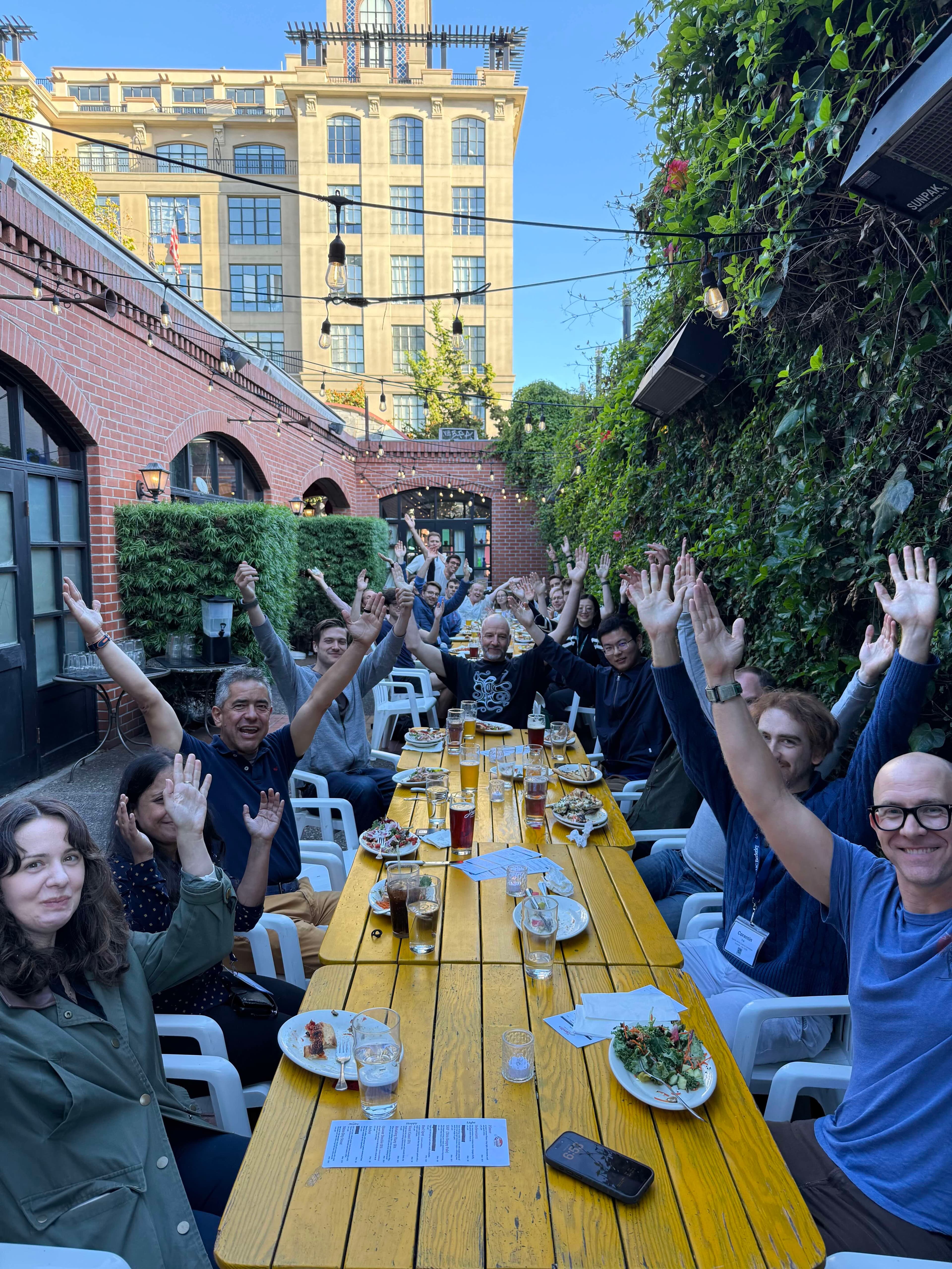 Attendees at the first AAI4Science Developer Summit raising their hands around a long outdoor dinner table in Berkeley
